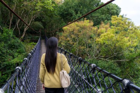 Téléchargez les photos : Femme marche le long du pont suspendu dans la forêt - en image libre de droit