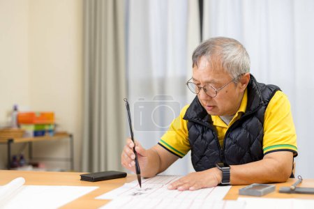 Téléchargez les photos : Asiatique vieil homme pratique chinois calligraphie personnage à la maison - en image libre de droit