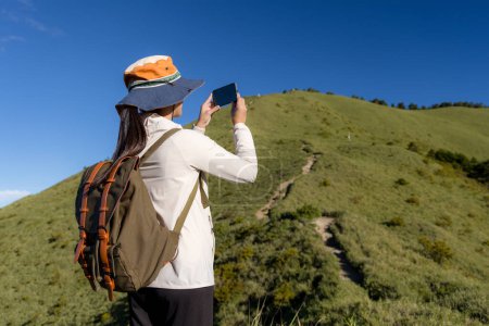Foto de Mujer senderista disfrutar de la hermosa vista y el uso del teléfono móvil para tomar una foto en el pico de la montaña - Imagen libre de derechos