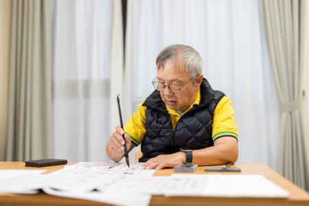 Foto de Asiático viejo hombre práctica chino caracteres con caligrafía en casa - Imagen libre de derechos