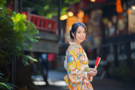Téléchargez les photos : Femme asiatique essayer de porter kimono japonais avec l'arrière-plan traditionnel du village japonais - en image libre de droit