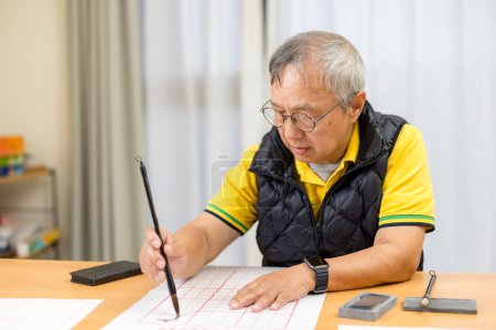 Photo for Asian old man write Chinese calligraphy character at home - Royalty Free Image