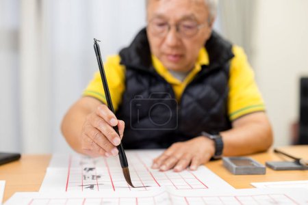 Photo for Asian old man practice Chinese characters with calligraphy at home - Royalty Free Image