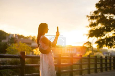 Foto de Mujer tomar fotos en el teléfono celular bajo el sol destello en el campo - Imagen libre de derechos