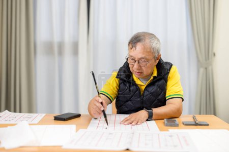 Téléchargez les photos : Asiatique vieil homme pratique caractères chinois avec calligraphie à la maison - en image libre de droit