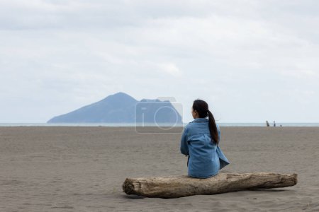 Téléchargez les photos : Femme assise sur la plage et regarder le Guishan à Yilan - en image libre de droit