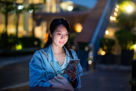 Photo for Woman look at mobile phone at outdoor in the evening time - Royalty Free Image