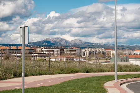 This vivid image portrays a contemporary urban landscape, showcasing residential buildings in the foreground with a majestic mountain range and wind turbines in the background.