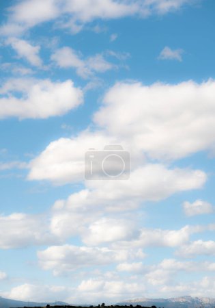 Nubes esponjosas derivan perezosamente a través del vasto cielo azul, creando un contraste dramático sobre un horizonte montañoso distante, capturando la naturaleza serena e ilimitada del paisaje..