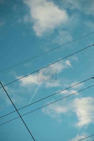A serene sky crossed by power lines and a high-flying jet's contrail, blending technology with nature's vastness.