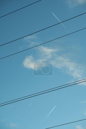 A serene sky crossed by power lines and a high-flying jet's contrail, blending technology with nature's vastness.