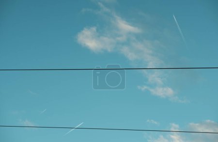 Stromleitungen schneiden sich durch einen blauen Himmel und kreuzen sich mit den empfindlichen Spuren, die Flugzeuge in der Höhe hinterlassen..