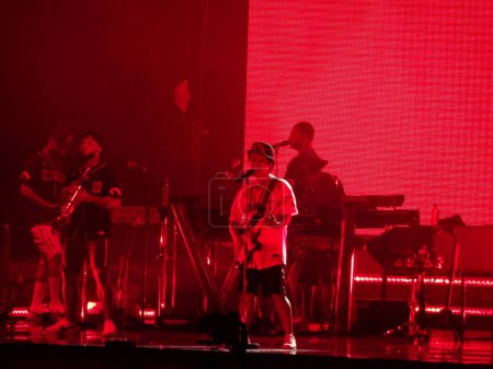 Photo for Honolulu - November 8, 2018:  Bruno Mars sings into mic and plays guitar as band plays on stage in red light during Concert in Hawaii at the Aloha Stadium. - Royalty Free Image