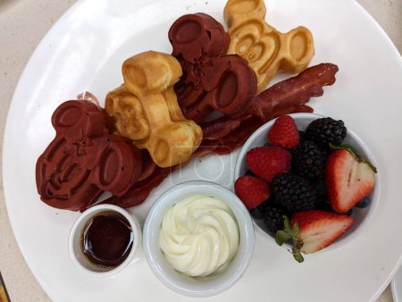 Honolulu - 14. Februar 2022: Genießen Sie ein köstliches Frühstück mit Micky-Maus-Waffeln, knusprigem Speck, frischen Erdbeeren und Brombeeren, garniert mit Sirup und Butter.