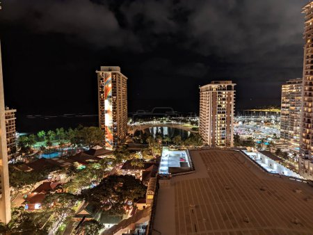 Foto de Waikiki - 24 de marzo de 2022: Vista aérea nocturna del Hilton Hawaiian Village en Waikiki, Hawaii. El hotel es un gran complejo de edificios altos con una laguna y piscina a lo largo del agua. Los edificios están brillantemente iluminados y la laguna está iluminada con - Imagen libre de derechos