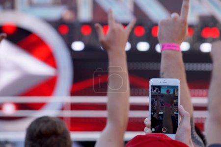 Téléchargez les photos : Santa Clara - 29 mars 2015 : Une personne tient un Iphone et enregistre des fans acclamant avec leurs bras en l'air lors d'un match de lutte. La personne est assise dans les gradins, et ils sont entourés par d'autres fans qui sont également acclamer et récor - en image libre de droit