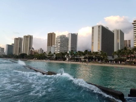 Téléchargez les photos : Waikiki - 27 mars 2017 : Waikiki en bord de mer serein avec des toits urbains en arrière-plan La ville de Waikiki est baignée de soleil crépusculaire, créant une scène belle et accueillante. - en image libre de droit