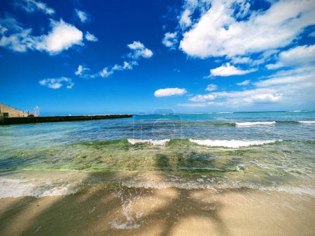 Kaimana Beach, also known as Sans Souci Beach, stretches gracefully alongside the iconic Waikiki Natatorium WWI War Memorial. The beach, once graced by legendary swimmers like Duke Kahanamoku and Johnny Weissmuller, invites visitors to bask in its ca