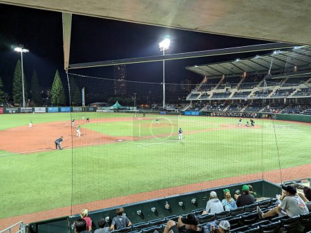 Foto de Honolulu - 15 de abril de 2023: Un partido de béisbol universitario de UH se desarrolla bajo las luces del estadio con los aficionados en primer plano. - Imagen libre de derechos