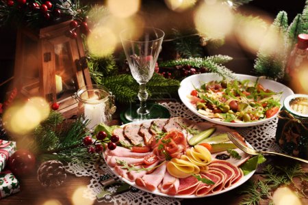 Christmas table with a platter of sliced ham, salami, cheese and cured meats and salad with vegetables, ham and arugula leaves