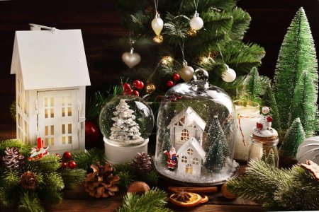 Téléchargez les photos : Décoration de Noël avec des décors en forme de maison blanche sous la cloche de verre, boule de neige et grande lanterne de maison sur la table - en image libre de droit