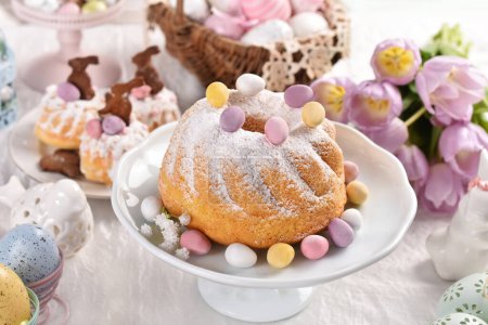 Foto de Traditional ring cakesprinkled with powdered sugar and muffins on Easter table in pastel colors - Imagen libre de derechos
