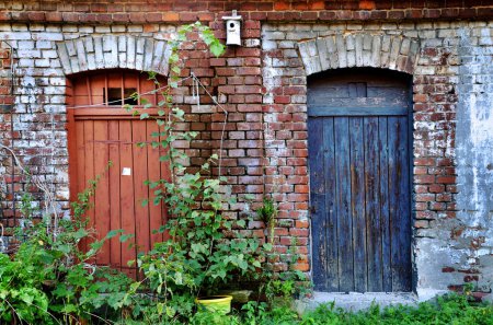 Brick building with two old doors in red and blue color of lumber-rooms or shed