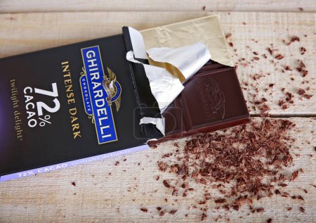 Photo for Overhead studio shot of a dark chocolate bar in the package with shavings on a wooden background unhealthy food concept - Royalty Free Image