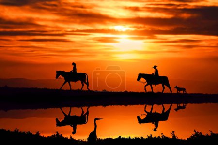 Photo for Two horse riders in front of a beautiful sunset with a dog trailing behind - Royalty Free Image