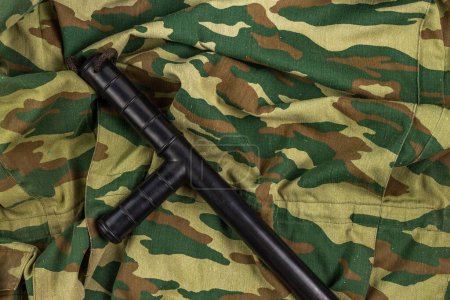 Photo for Black rubber baton on old Russian camouflage background, high angle view. - Royalty Free Image