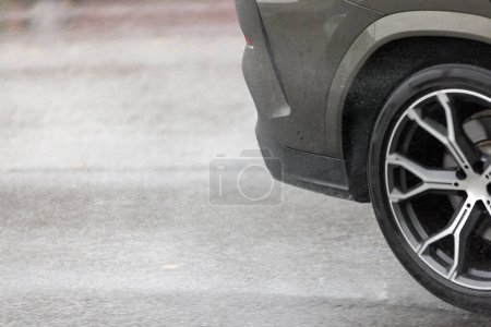 Regenwasser spritzt aus Rädern eines grauen Autos, das sich schnell auf Asphaltstraße bewegt.