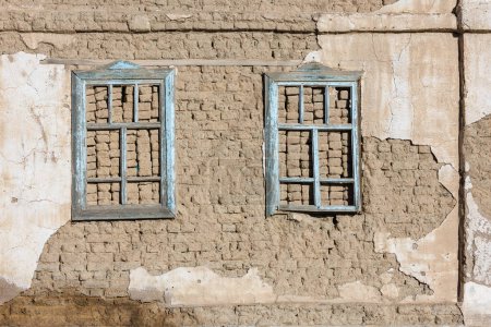Téléchargez les photos : Vieux mur de briques d'air de maison adobe avec deux cadres de fenêtre en bois intégrés et les restes de plâtre pelés texture plate et fond plein cadre. - en image libre de droit