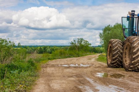 Tractor with large wheels on the edge of a dirt road at summer day with cloudy sky, copy space composition