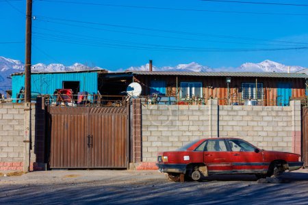 Foto de Coche rojo sin ruedas delante de la valla de ladrillo del depósito de chatarra, afuera en la tarde soleada. - Imagen libre de derechos