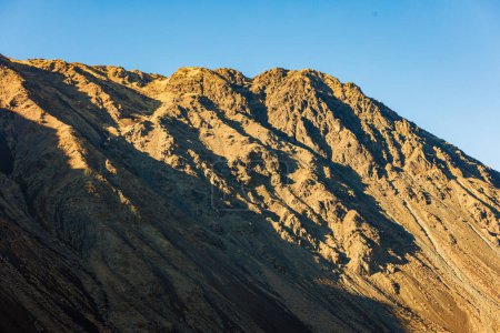Téléchargez les photos : Paysage naturel offrant une vue rapprochée sur une pente de flanc de montagne sous la lumière directe du soleil du soir avec ciel bleu clair au-dessus. - en image libre de droit