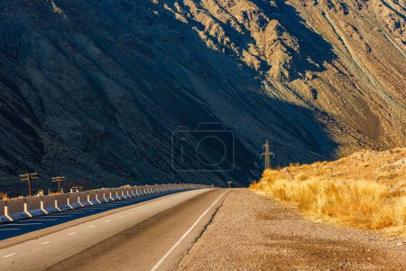 Téléchargez les photos : Une autoroute vide s'étend à travers un paysage naturel avec la montagne en arrière-plan, mettant en valeur la surface de la route asphaltée comme il serpente à travers le terrain vallonné. - en image libre de droit