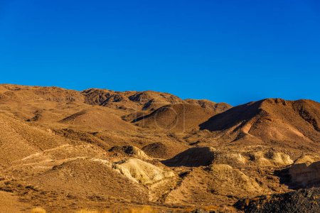 Kirgisische Landschaft mit einem Gebirge, das sich vor einem klaren blauen Himmel erhebt. Die ausgetrockneten Wiesen und sanften Hänge schaffen einen natürlichen Horizont