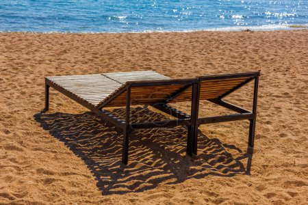 Dos sillas de salón al aire libre vacías en la playa de arena cerca del agua azul en el día soleado fuera de temporada.