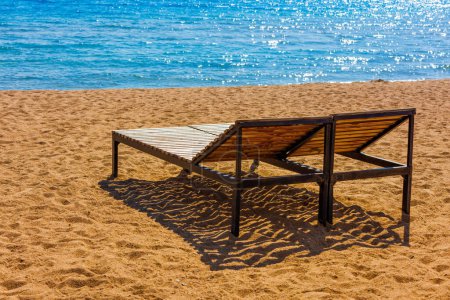 Deux chaises longues extérieures vides sur la plage de sable près de l'eau bleue à la journée ensoleillée hors saison.