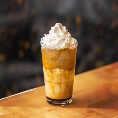 Caramel latte coffee in a tall glass with syrup and whipped cream.