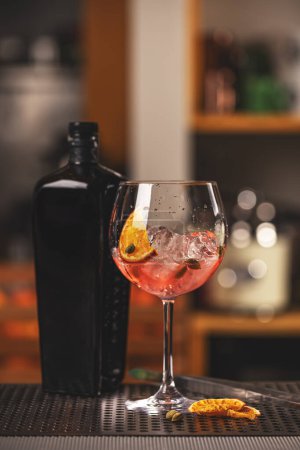 Pink gin cocktail served in balloon glass with ice cube and orange slice