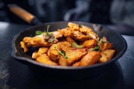 Fried potato wedges with schnitzel served in iron pan, close up