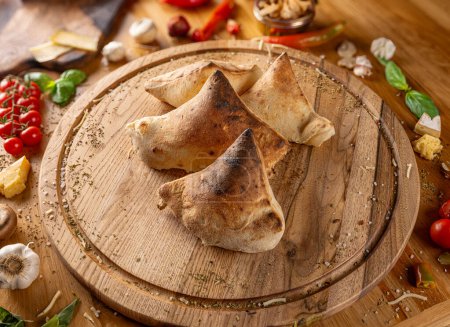 Photo for Delicious calzones on a wooden board surrounded by fresh ingredients - Royalty Free Image