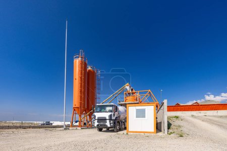 Concrete batching plant with a mixing tower and cement truck parked under a clear sky