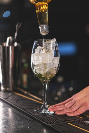 Primer plano de un camarero vertiendo un líquido dorado en un vaso con cubitos de hielo en un bar