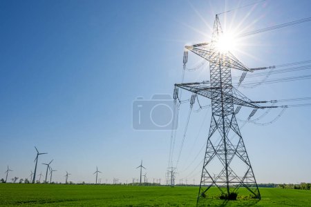 Ein Strommast mit der Sonne im Hintergrund und Windrädern im Hintergrund in Deutschland