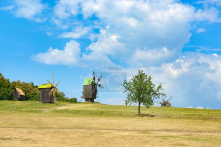 Old wooden mills on hill against background bright blue sky.