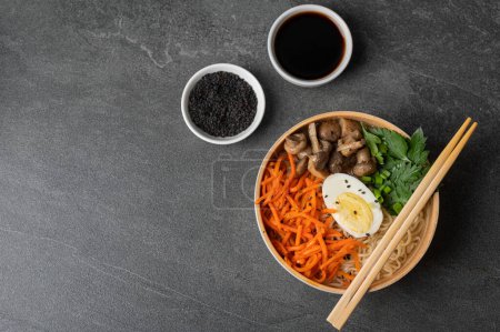 Téléchargez les photos : Soupe de nouilles, ramen dans un bol blanc (bol) avec oeuf de poulet, carottes, champignons sur fond de pierre d'ardoise sombre. Asiatique traditionnel fast food - en image libre de droit