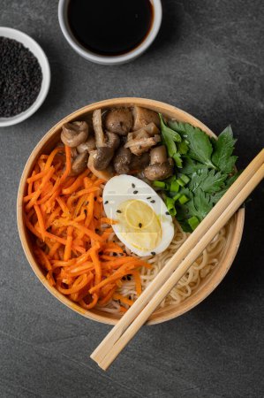 Téléchargez les photos : Soupe de nouilles, ramen dans un bol blanc (bol) avec oeuf de poulet, carottes, champignons sur fond de pierre d'ardoise sombre. Asiatique traditionnel fast food - en image libre de droit