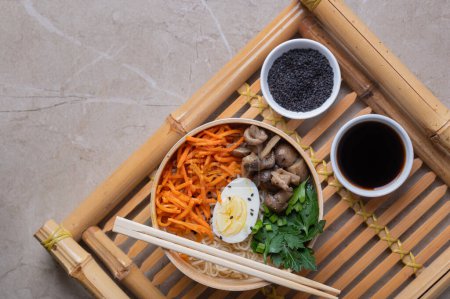 Photo for Noodle soup, ramen in a white bowl (bowl) with chicken egg, carrots, mushrooms on a bamboo tray on a light stone background. Asian traditional fast food - Royalty Free Image